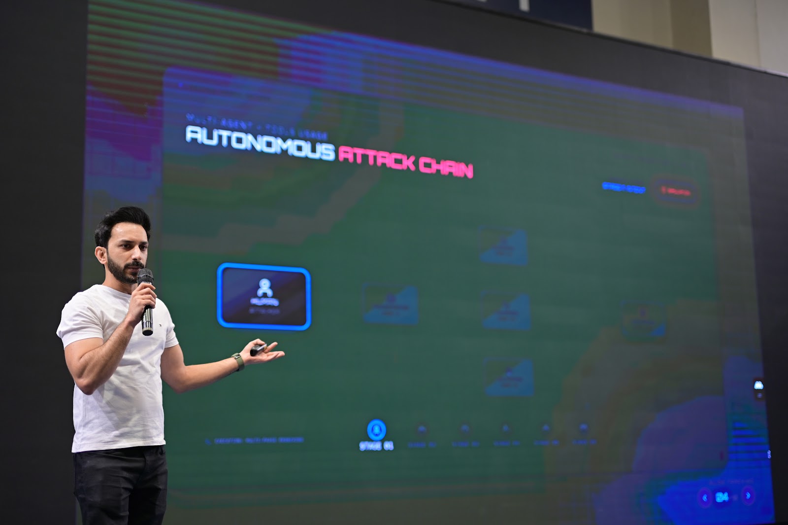 Atompoint presenter speaking in front of digital screen displaying Autonomous Attack Chain security architecture diagram